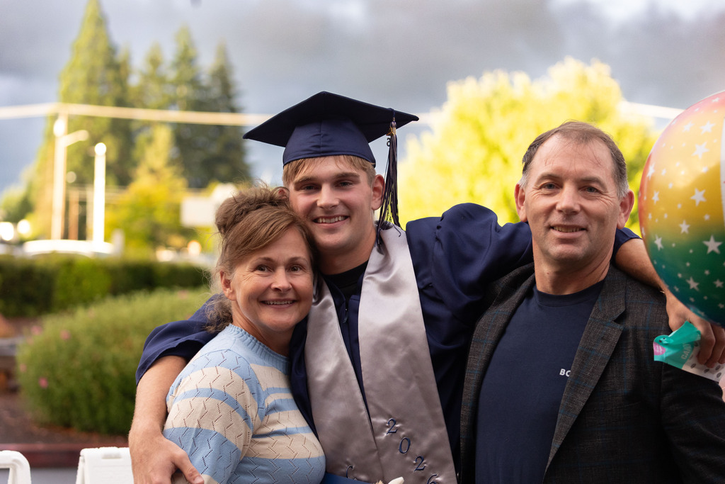 A man and his mom and dad smiling outside with a cloudy sky