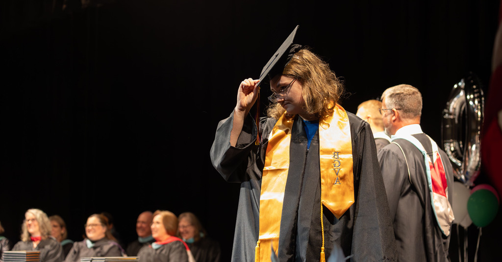 A young graduate tips his hat on stage