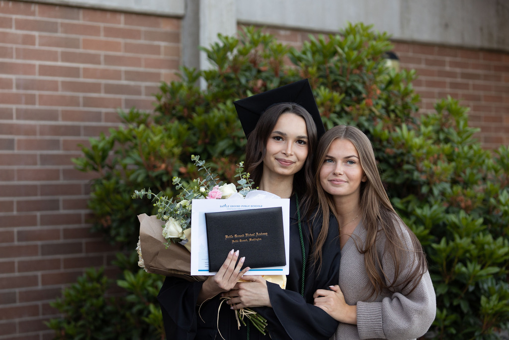A young woman holds her flowers, graduation diploma, seal of biliteracy.