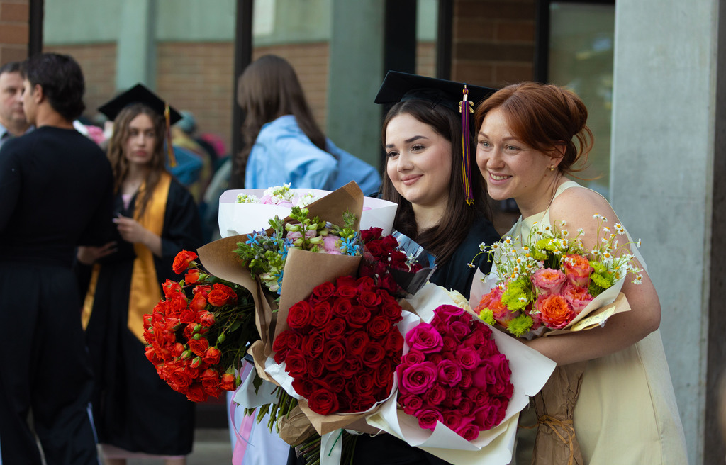 A young woman and a graduate hold an enormous amount of flowers