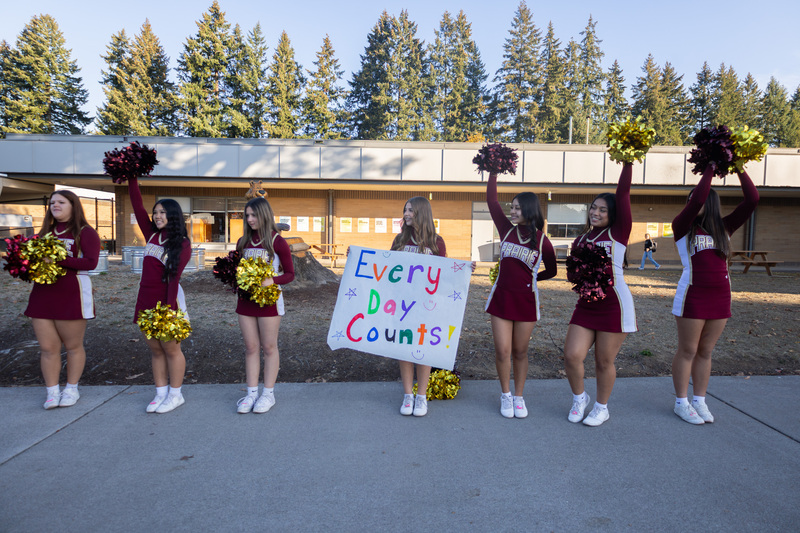 cheerleaders hold signs and welcome young students to school