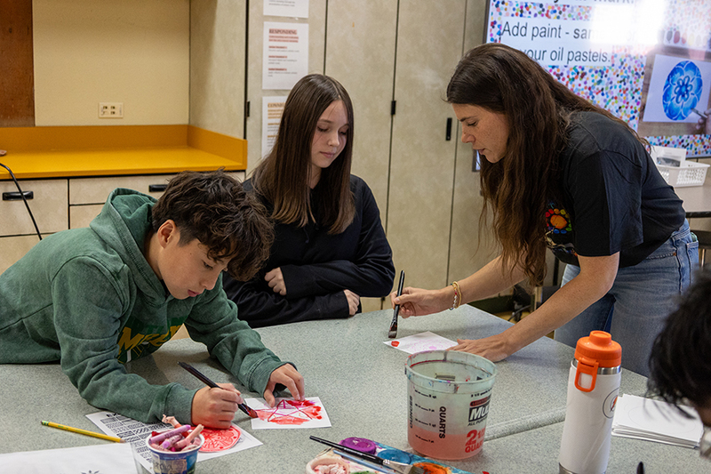 teacher showing two students how to paint