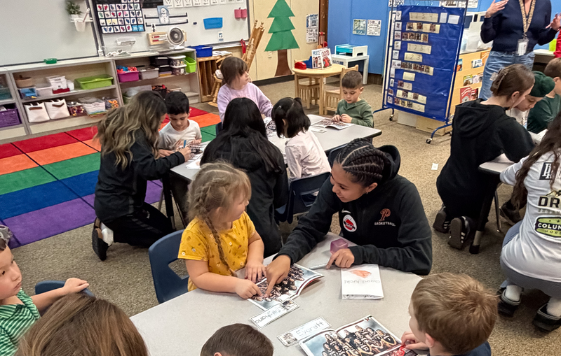a group of teen basketball players reading to young ones