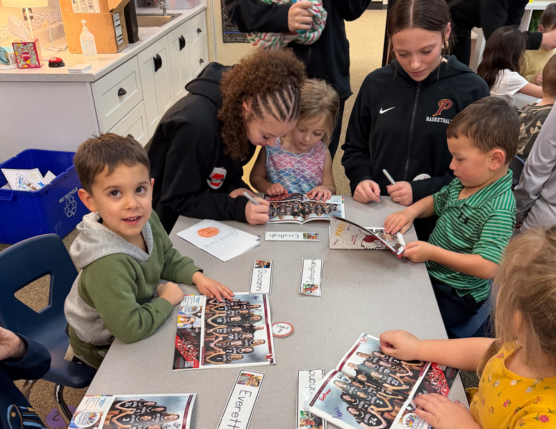 a group of teen basketball players reading to young ones