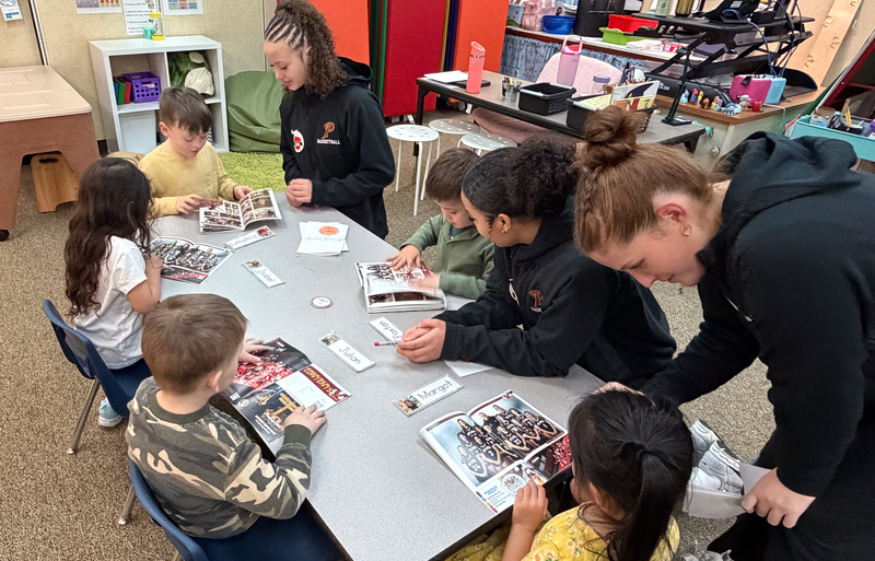 a group of teen basketball players reading to young ones