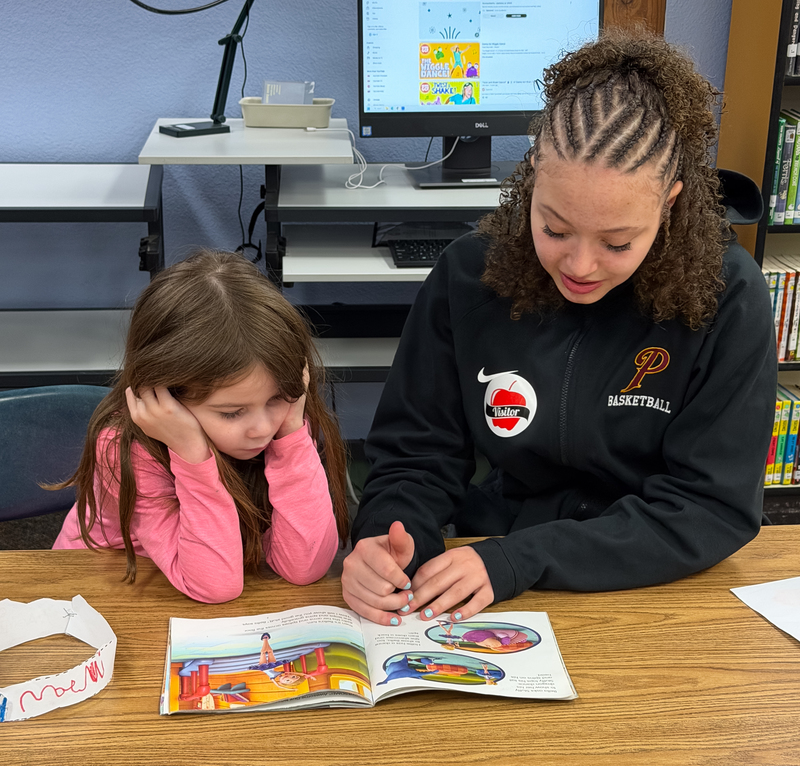 a group of teen basketball players reading to young ones