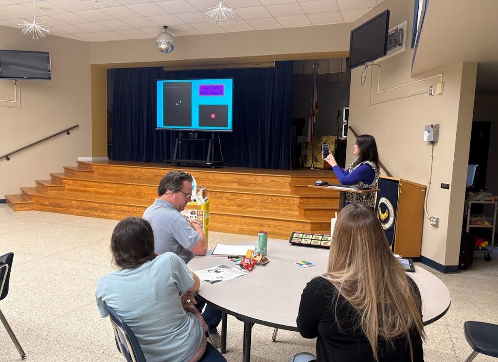 Parents sit at a table while a staff member presents at the front of the room, using a large screen during a school IEP support session.