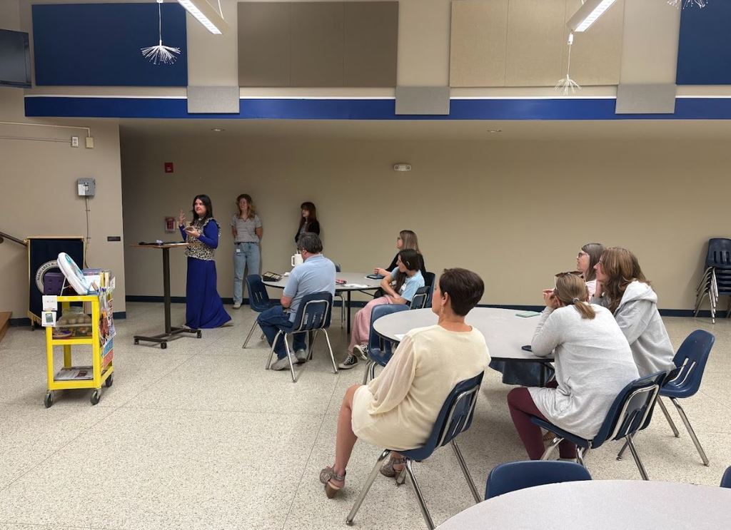 Families sit at round tables listening as a presenter speaks at the front of the room during a parent workshop on supporting students with IEPs.
