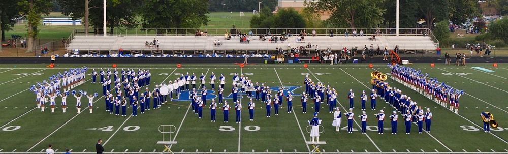 A marching band photo of students in blue uniforms on a football field.