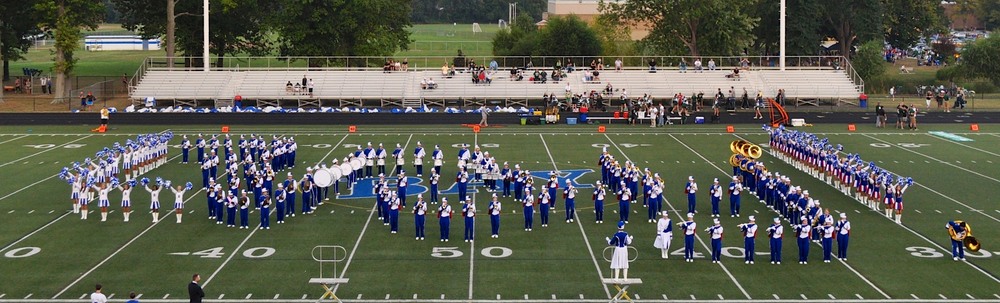 A marching band photo of students in blue uniforms on a football field.