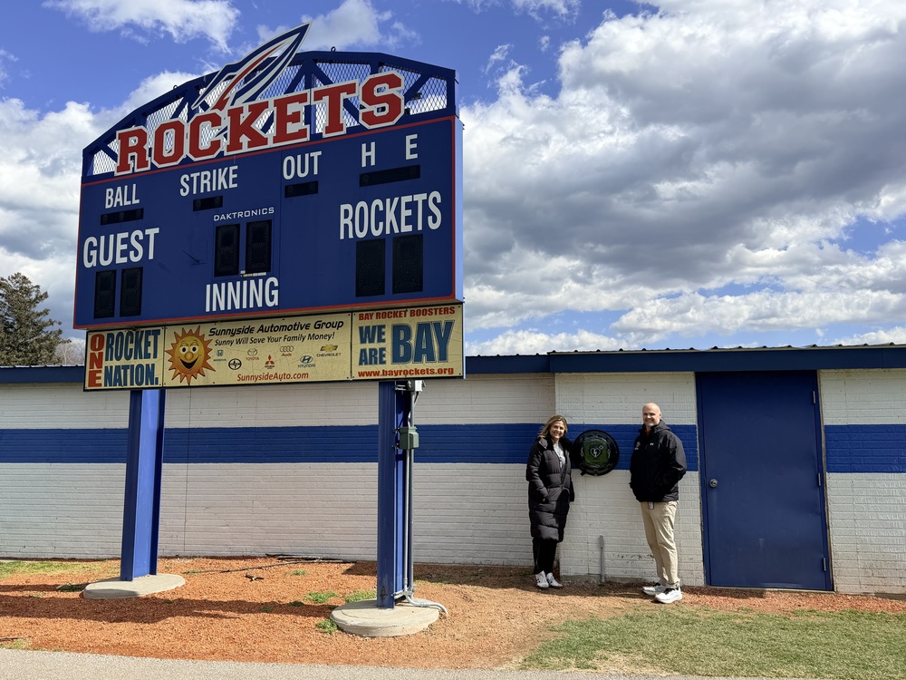 New AED located at Bay High School baseball diamond photo with Nurse Val and AD Matt Spellman by the signboard