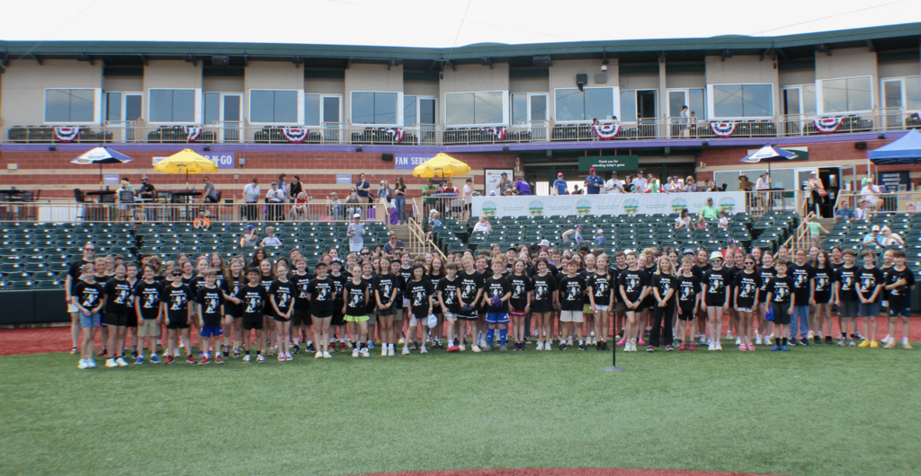 Westerly fourth-grade chorus performs at a Crushers baseball game with stands in the background.