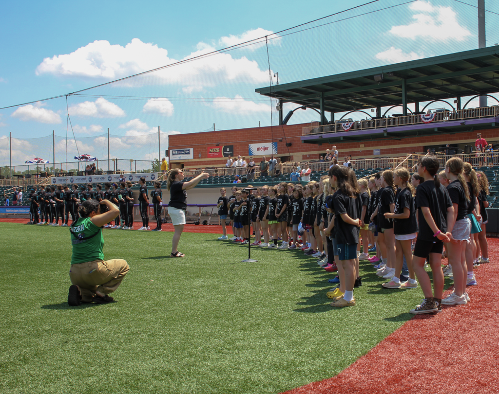 Westerly fourth-grade chorus performs at a Crushers baseball game with stands in the background.