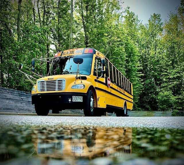 An image of a Bay Village yellow school bus parked with a reflection of it in a puddle.
