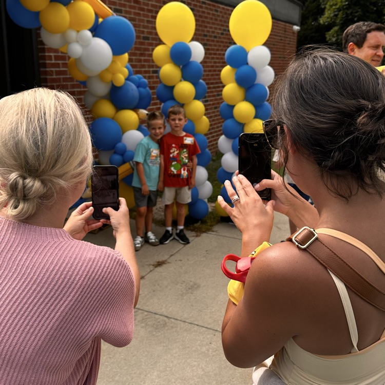 two mom’s taking a photo of their students in front of a balloon arch