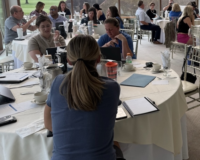 Members of the school district's leadership team are seated around tables, taking notes and talking about their profressional development session.