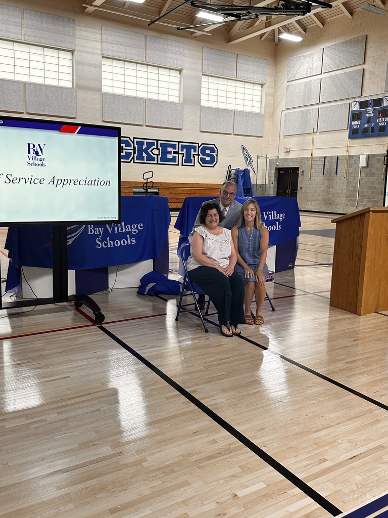 The supt and two teachers are seated in the gym as the two teachers are honored for their years of service.