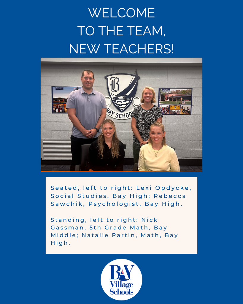 Four new teachers seated and standing behind a desk, smiling at their orientation for the new school year.