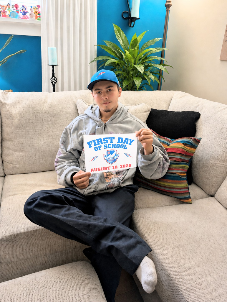 A high school male student sitting on a couch holding a first day of school photo.