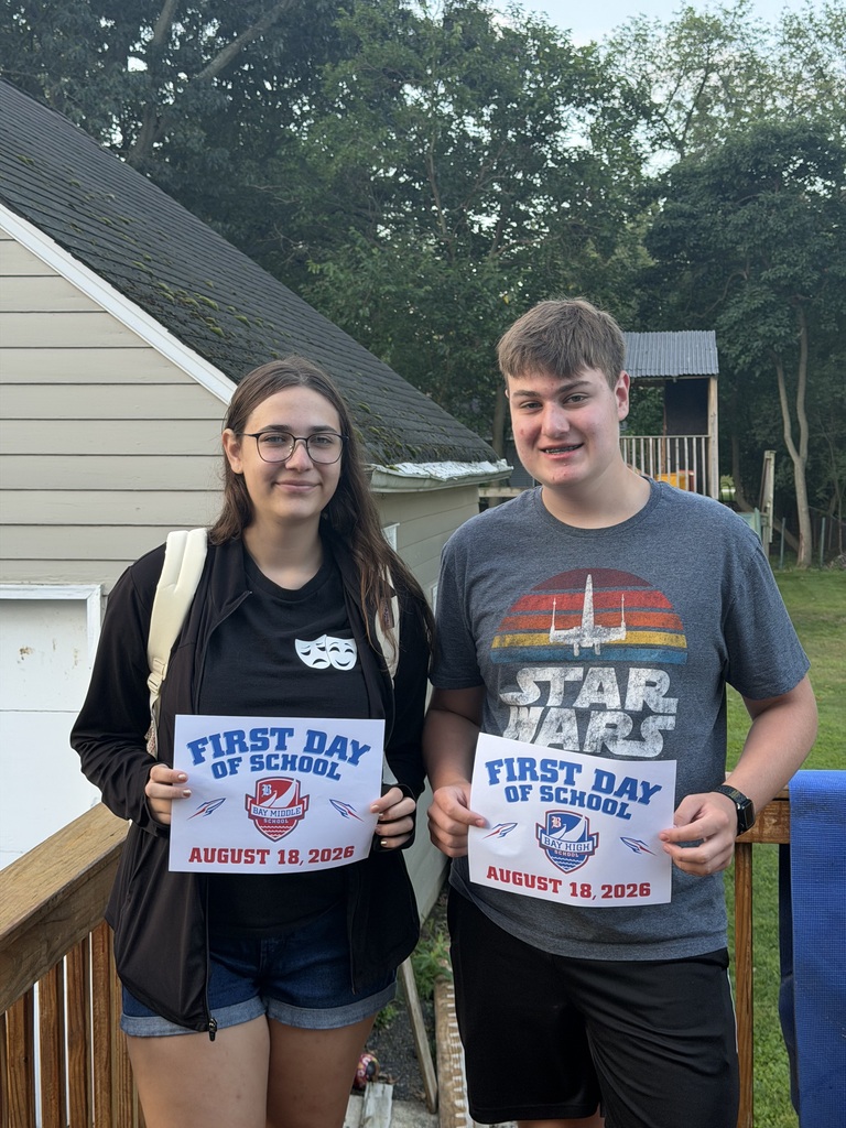 A brother and sister outside on the porch holding first day of school signs. They are in middle school and high school.
