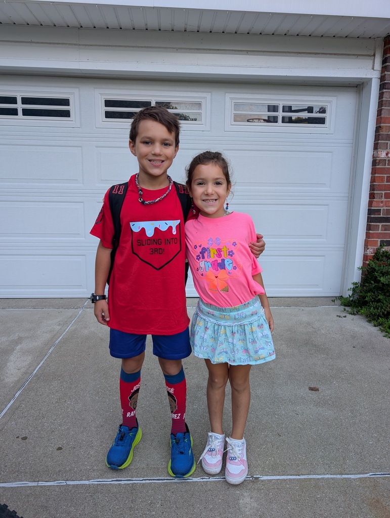 A brother and sister standing inside their white garage door on the first day of elementary school.