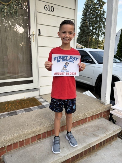 An elementary-aged boy standing on his front porch holding a first day of school sign.