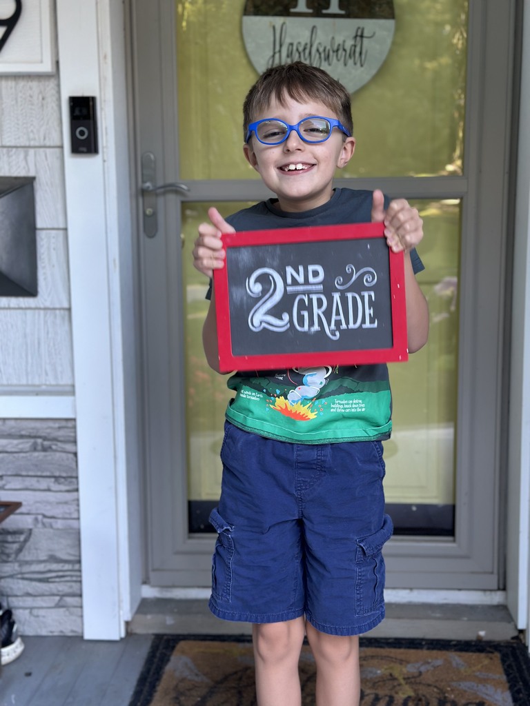 An elementary-aged boy standing on his front porch holding a first day of school sign.