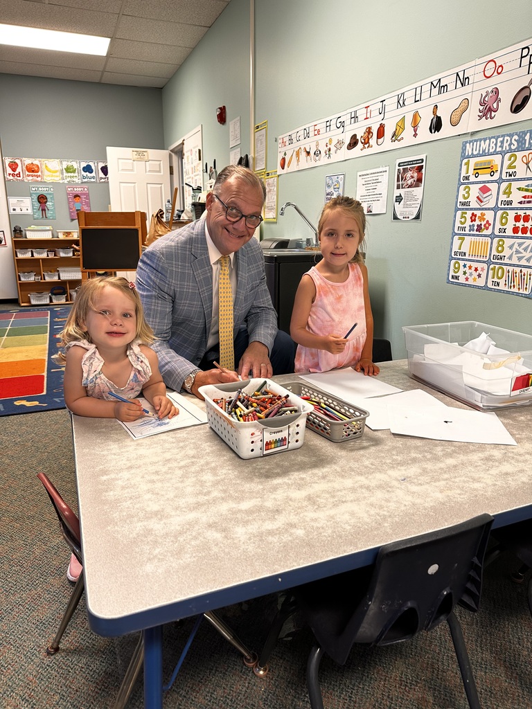 The superintendent coloring with two pre-K students, all seated at a table in a classroom.