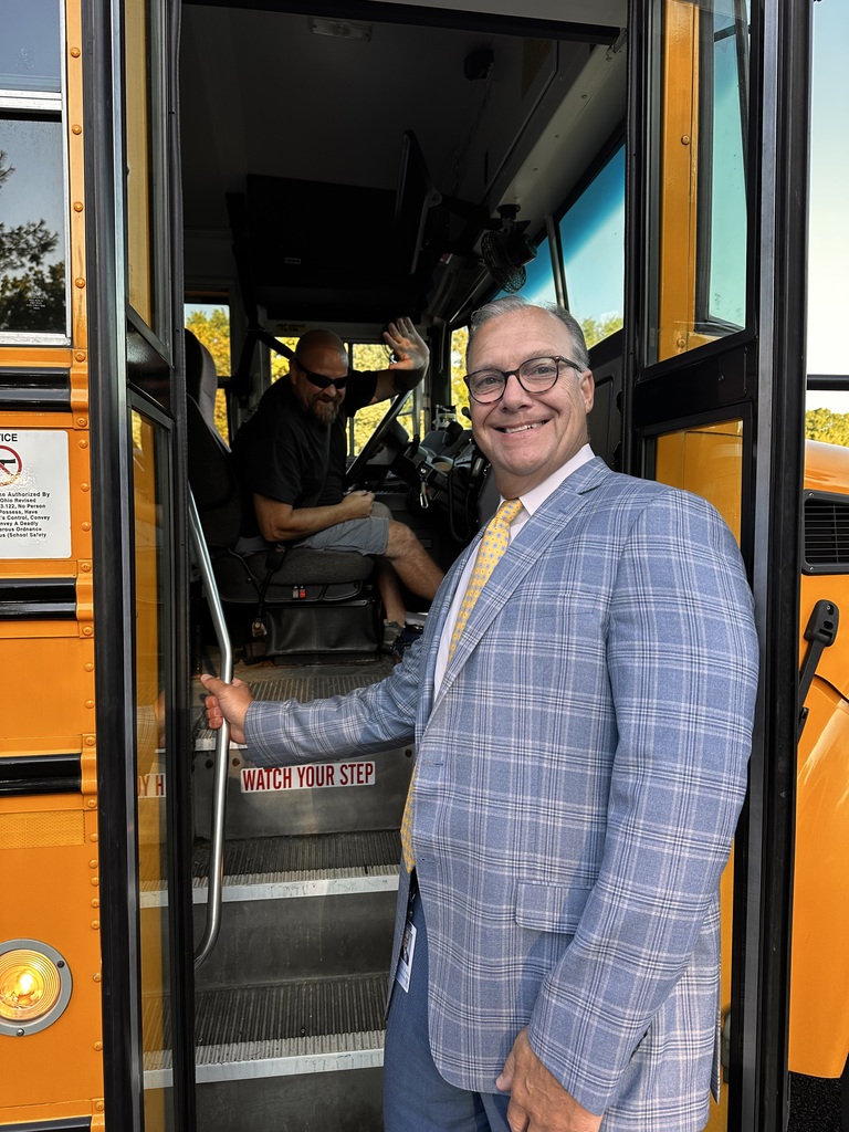 The superintendent poses with a school bus driver. They are both smiling and waving on the first day of school.