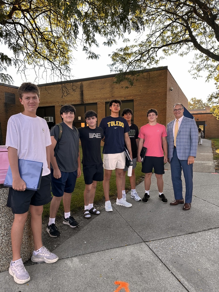 Six high school students stand outside their school, posed with the superintendent on the first day of school. 