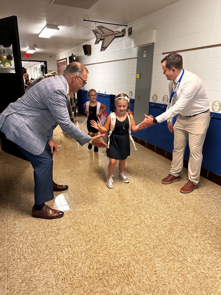 An elementary school student does double high-fives with the superintendent and her principal in the hallway of her school. 