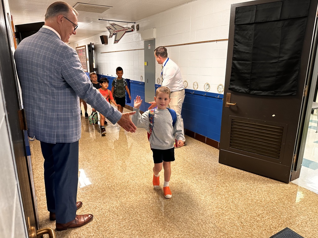 An elementary student is giving a high-five to his superintendent in the hallway of his school on the first day of school. 