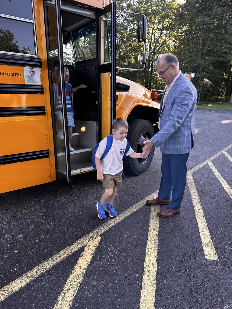 An elementary student gets off the bus on his first day of school to give his superintendent a high-five before he enters the building.