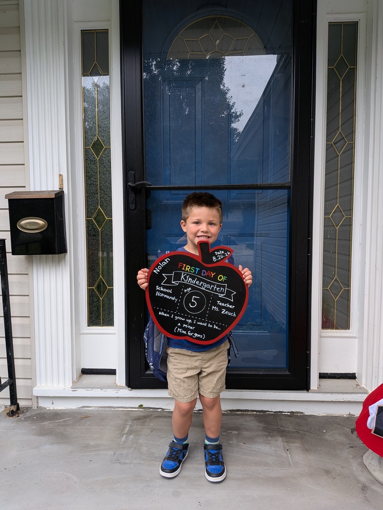 A kindergarten student standing on his front porch holding a first day of school sign.