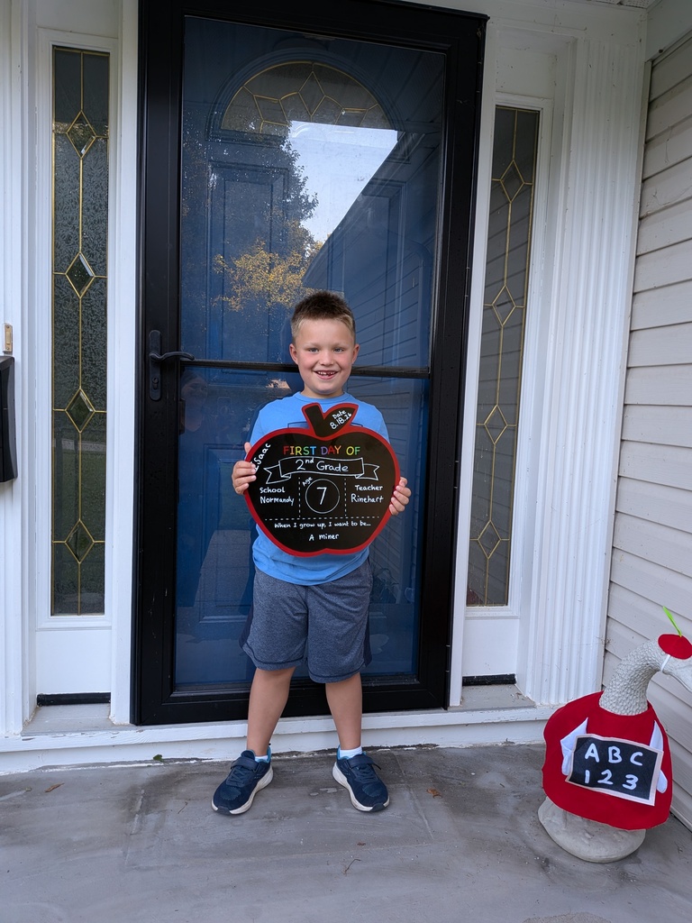 An elementary school student standing on his front porch with a first day of school sign.