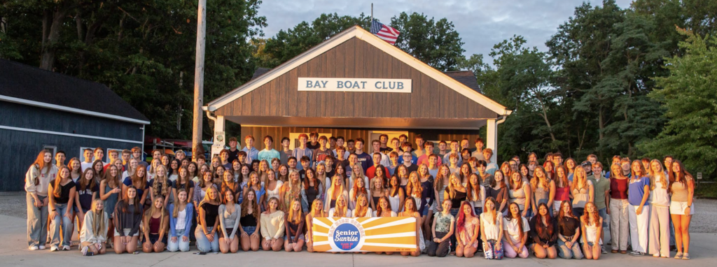 The class of 2027 kneeling and standing in front of the Bay Boat Club at sunrise on the first day of school.