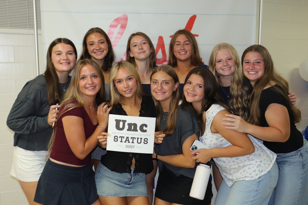 Senior girls in the hallway of their high school posing in front of a last first day of school sign.
