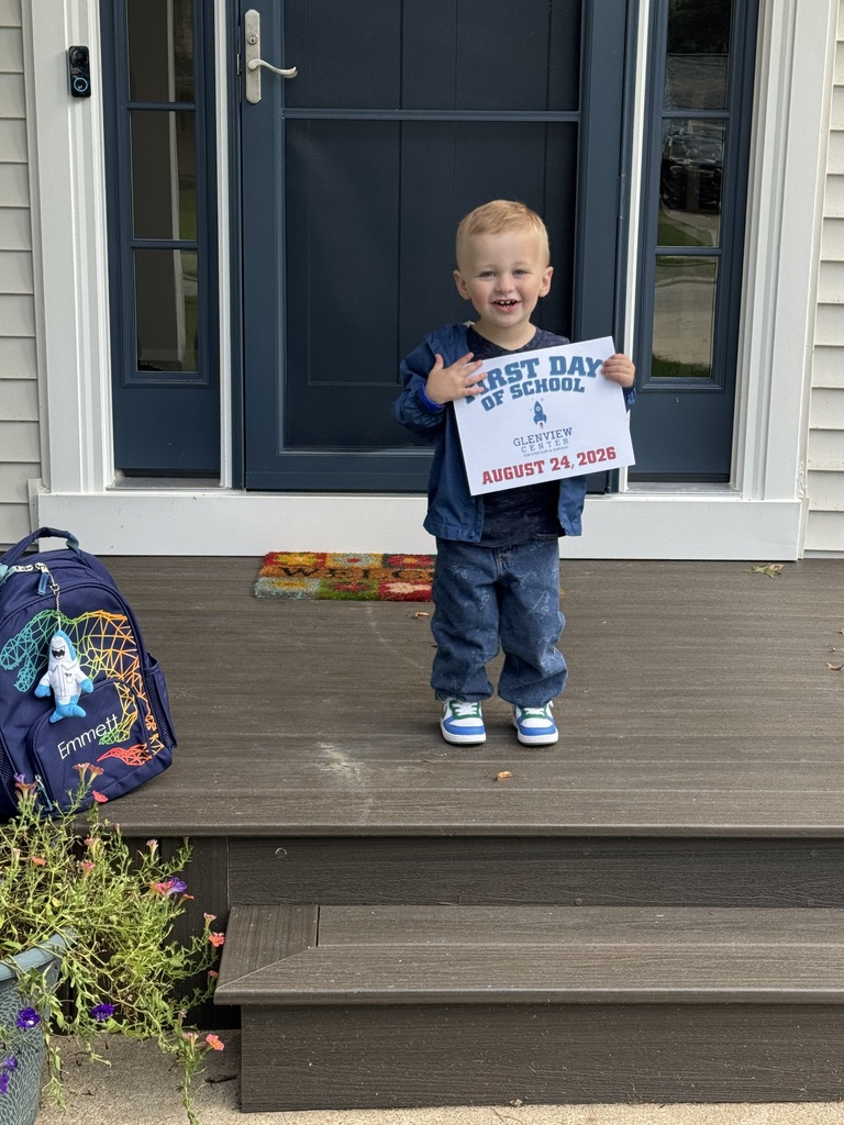 A preschool boy standing in front of his front door holding a first day of school sign for preschool. 