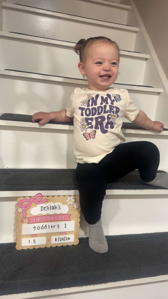 A photo of a toddler seated on a step with her first day of school sign for toddlers.