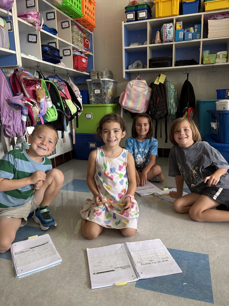 Four first-graders sitting on the floor of their classroom doing a math activity in a small group.