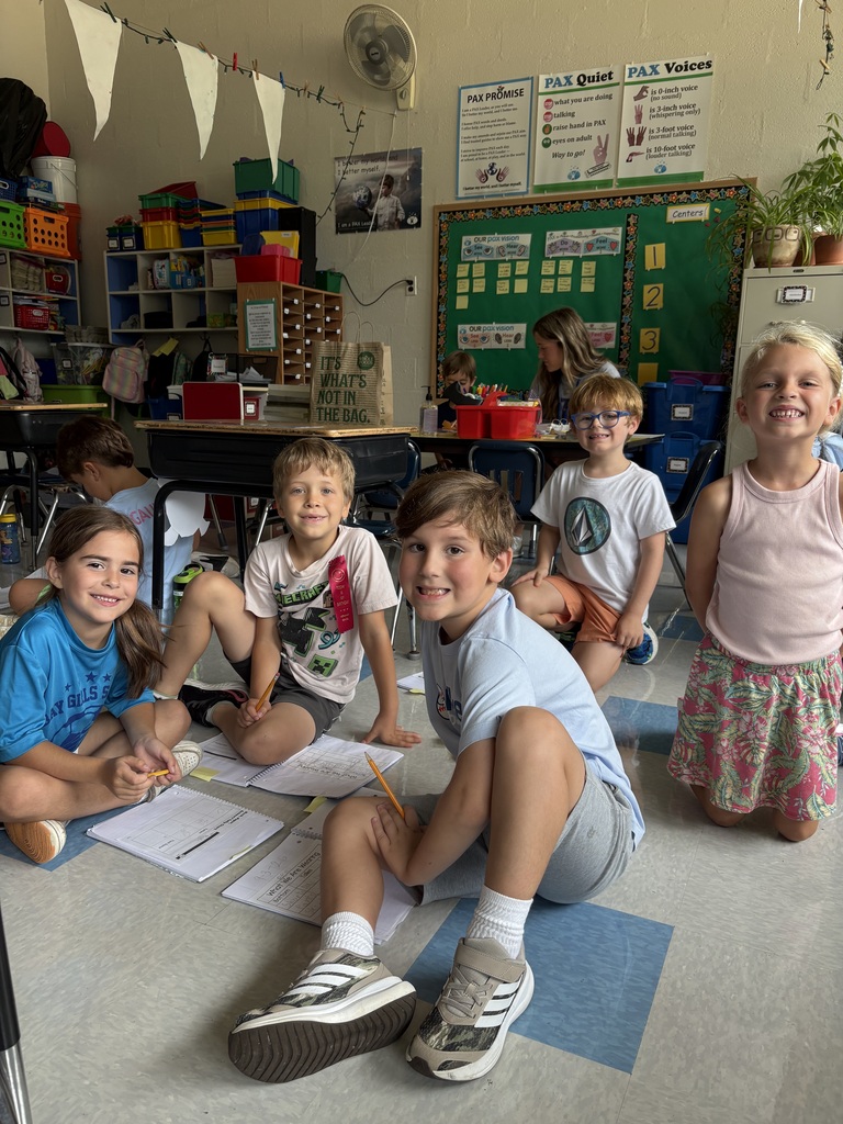 Five first-graders sitting on the floor in their classroom working on a collaborative math project.