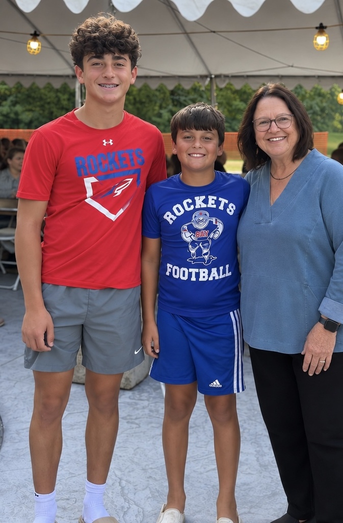 District grandparent Debbie Callihan with her two grandsons standing under a white tent with their red, white and blue spirit wear on.