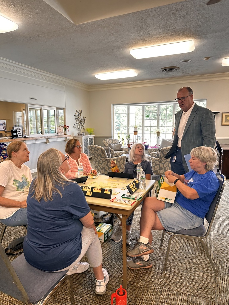 A man standing, talks to a small group of senior citizen ladies while they play a game.