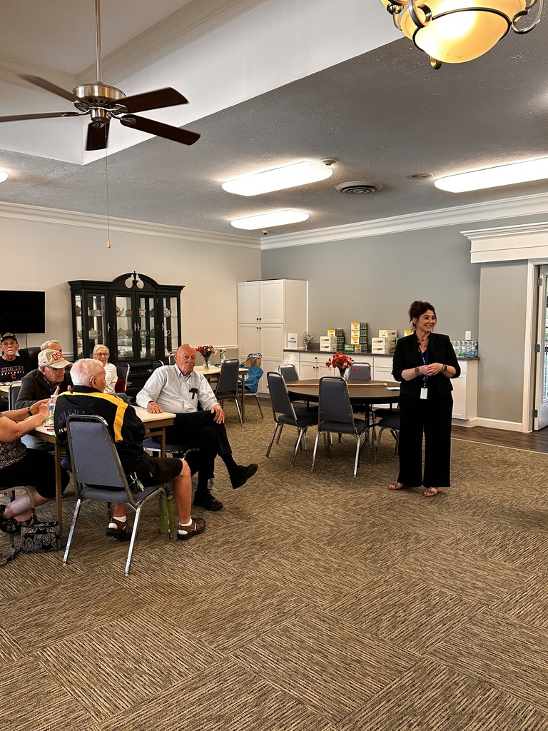 A woman talks to a room full of senior citizens seated at tables.