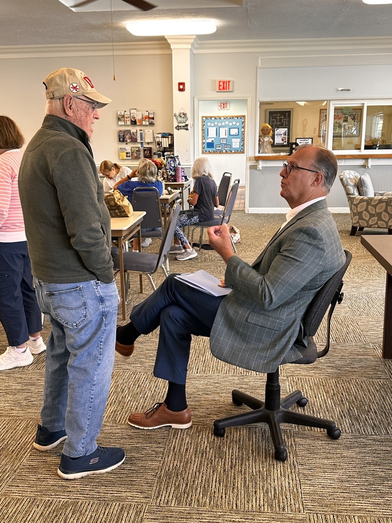 Two mean, one standing and one seated, have a conversation at the senior center.