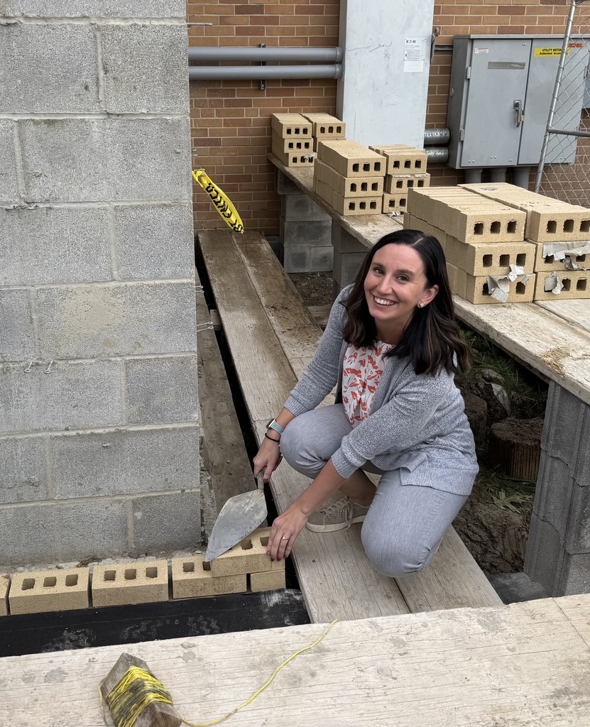 A smiling woman, the Glenview Center Director, lays the first bricks in the foundation at Glenview Center amongst the construction site.
