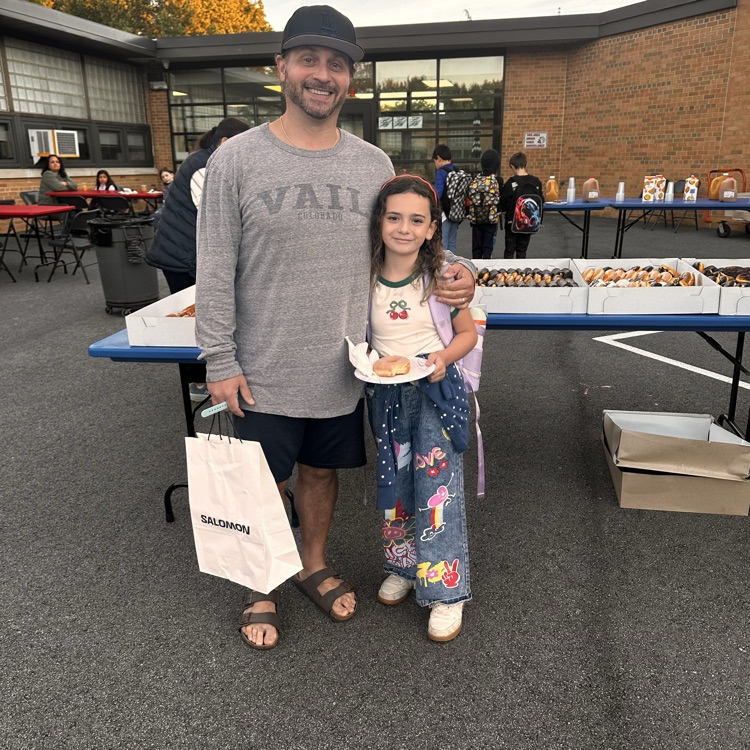 A man in his elementary school daughter arrive to A morning event with donuts in the background