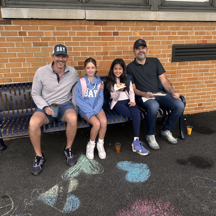 to Dads and their daughter sitting on a bench at a school morning event