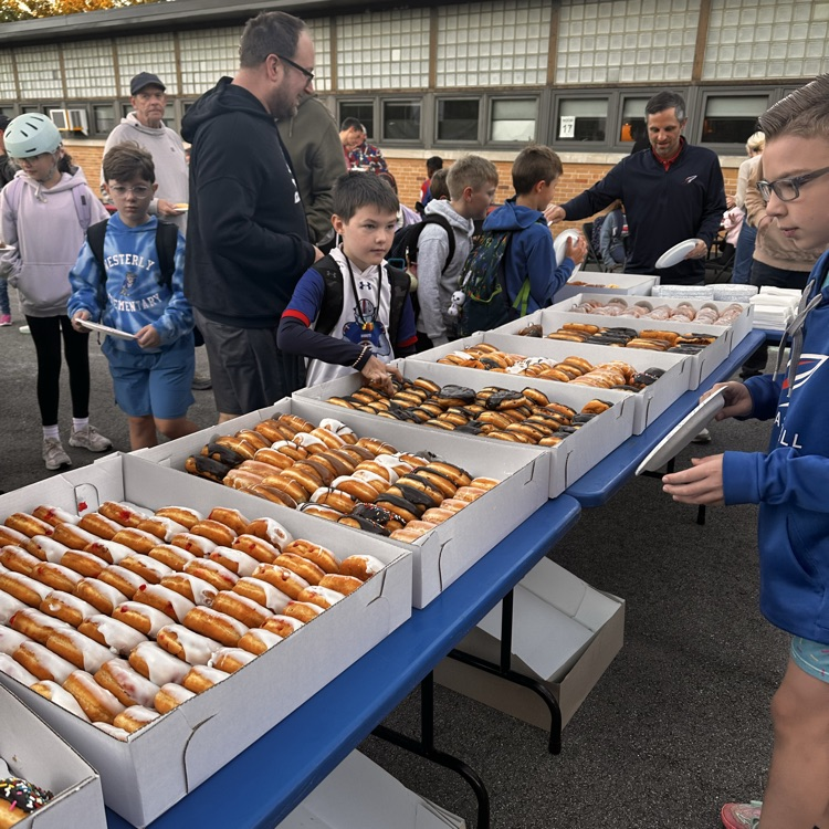 A table with a box of donuts on it with a student choosing one.