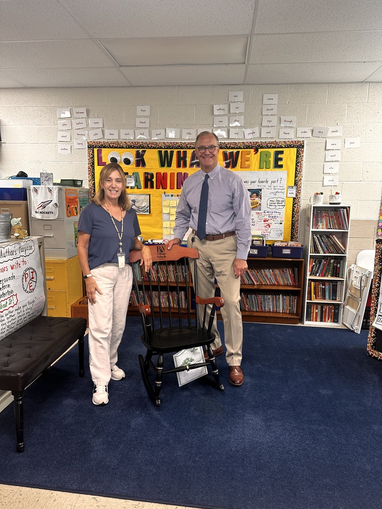 A teacher and a superintendent flank a rocking chair in the teacher's classroom.